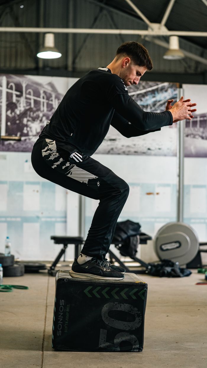 Young male athlete doing box jump exercise in gym setting.